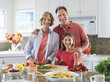 Photo: Family standing beside kitchen worktop, woman chopping tomatoes, smiling, front view, portrait Family standing beside kitchen worktop, woman chopping tomatoes, smiling, front view, portrait