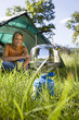 Photo: Young woman sitting inside dome tent in woodland clearing, waiting for kettle to boil on camping stove, smiling (surface level) Young woman sitting inside dome tent in woodland clearing, waiting for kettle to boil on camping stove, smiling (surface level)