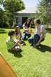 Family taking break from assembling tent on garden lawn, mother serving orange juice, smiling