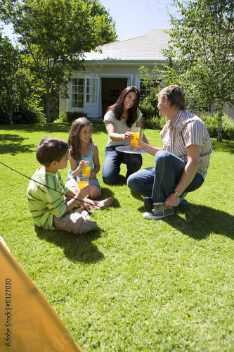 Photo: Family taking break from assembling tent on garden lawn, mother serving orange juice, smiling Family taking break from assembling tent on garden lawn, mother serving orange juice, smiling