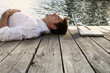 A young man with a laptop laying on a wooden jetty