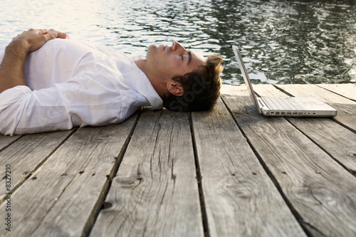 Photo: A young man with a laptop laying on a wooden jetty A young man with a laptop laying on a wooden jetty