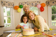 Photo: Girl (4-6) sitting with mother and grandmother at table beside birthday cake, smiling, portrait Girl (4-6) sitting with mother and grandmother at table beside birthday cake, smiling, portrait