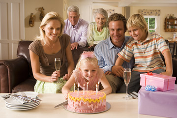 Photo: Three generation family sitting on sofa at home, girl (4-6) blowing out candles on birthday cake Three generation family sitting on sofa at home, girl (4-6) blowing out candles on birthday cake