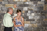 Photo: Mature man flirting with younger woman beside stone wall, holding glasses of white wine, woman looking away Mature man flirting with younger woman beside stone wall, holding glasses of white wine, woman looking away