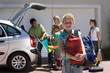 Photo: Family loading camping equipment into parked car boot on driveway, girl (8-10) carrying rucksack and sleeping bag in foreground, smiling, portrait Family loading camping equipment into parked car boot on driveway, girl (8-10) carrying rucksack and sleeping bag in foreground, smiling, portrait