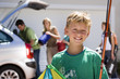Photo: Family loading camping equipment into parked car boot on driveway, focus on boy (8-10) carrying fishing rod and kite in foreground, smiling, portrait Family loading camping equipment into parked car boot on driveway, focus on boy (8-10) carrying fishing rod and kite in foreground, smiling, portrait