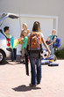 Photo: Family loading camping equipment into parked car boot on driveway, girl (11-13) carrying rucksack, soccer ball and tennis racquets in foreground, rear view Family loading camping equipment into parked car boot on driveway, girl (11-13) carrying rucksack, soccer ball and tennis racquets in foreground, rear view