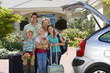 Photo: Family standing with luggage beside open boot of parked car on driveway, children (8-10) holding cuddly toys, smiling, portrait Family standing with luggage beside open boot of parked car on driveway, children (8-10) holding cuddly toys, smiling, portrait