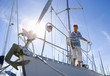 Man standing on deck of moored sailing boat, holding rope (lens flare)