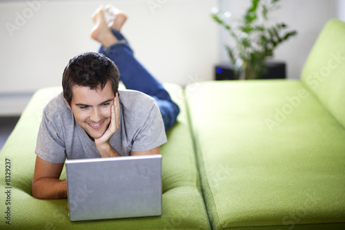 Photo: Young man with a laptop, laying on a bed Young man with a laptop, laying on a bed