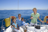 Photo: Family relaxing on deck of sailing boat out at sea, mother standing at helm, steering, smiling, portrait Family relaxing on deck of sailing boat out at sea, mother standing at helm, steering, smiling, portrait