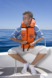 Photo: Man sitting at stern of sailing boat out at sea, wearing orange life jacket, tying strap, smiling Man sitting at stern of sailing boat out at sea, wearing orange life jacket, tying strap, smiling