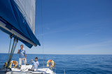 Photo: Father and son (8-10) standing at helm of sailing boat out to sea, boy steering, smiling Father and son (8-10) standing at helm of sailing boat out to sea, boy steering, smiling