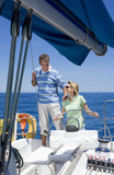Photo: Couple standing at helm of sailing boat out to sea, woman steering, man placing hand on woman’s shoulder, smiling Couple standing at helm of sailing boat out to sea, woman steering, man placing hand on woman’s shoulder, smiling