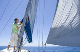 Photo: Man standing on deck of sailing boat out to sea, adjusting sail mast rigging, side view Man standing on deck of sailing boat out to sea, adjusting sail mast rigging, side view