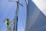 Photo: Father and son (8-10) standing on deck of sailing boat, adjusting sail mast rigging, side view, low angle view Father and son (8-10) standing on deck of sailing boat, adjusting sail mast rigging, side view, low angle view