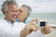 Foto: A senior couple on a beach taking a picture with a digital camera A senior couple on a beach taking a picture with a digital camera