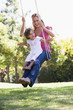 Woman and young girl outdoors on tree swing smiling
