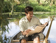 Young man sitting in a boat reading a newspaper