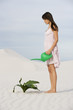 A woman watering a plant in the sand