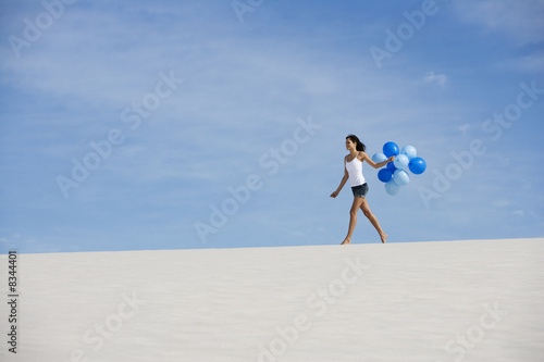 Photo: A woman walking in the desert holding a bunch of balloons A woman walking in the desert holding a bunch of balloons
