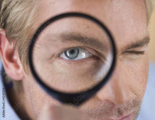 Photo: A young man looking through a magnifying glass A young man looking through a magnifying glass