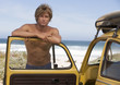 A young man leaning on the door of a car