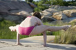 A woman performing youga exersizes on a rocky lake shore
