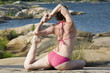 A woman performing youga exersizes on a rocky lake shore
