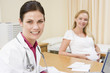 Doctor with laptop and pregnant woman in doctor's office smiling