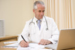Doctor using laptop and writing in doctor's office