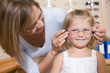 Photographie : Woman trying eyeglasses on young girl at optometrists smiling