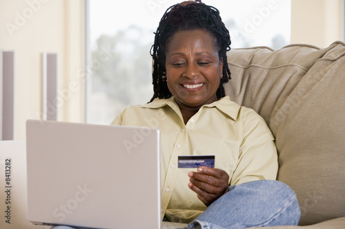 Photo: Woman in living room using laptop holding credit card and smilin Woman in living room using laptop holding credit card and smilin