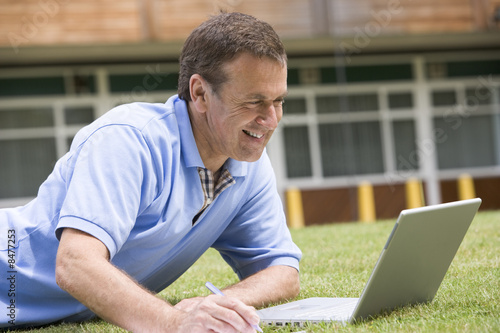 Photo: Man using laptop while lying in grass on campus Man using laptop while lying in grass on campus