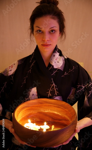 Photo: Young woman holding wooden bowl with burning candles Young woman holding wooden bowl with burning candles