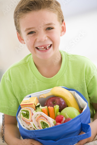 Photo: Young boy holding packed lunch in living room smiling Young boy holding packed lunch in living room smiling