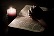 Praying hands on top of bible, lit by candle light Praying hands on top of bible, lit by candle light