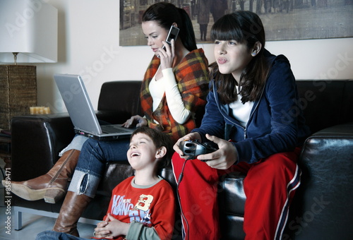 Photo: Mother works on laptop while children play video game Mother works on laptop while children play video game