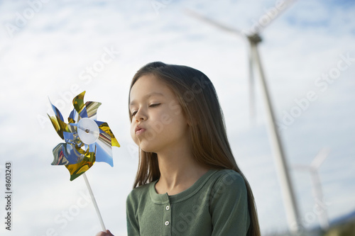 Photo: Girl 5-6 blowing toy windmill at wind farm Girl 5-6 blowing toy windmill at wind farm