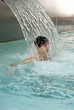 Young man standing under water spray in spa pool