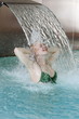 Young woman standing under water spray in spa pool