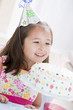 Young girl wearing party hat looking at birthday cake smiling