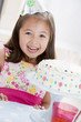 Photo: Young girl wearing party hat with birthday cake smiling Young girl wearing party hat with birthday cake smiling