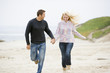 Photo: Couple running at beach holding hands smiling Couple running at beach holding hands smiling