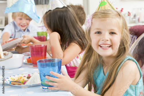 Photo: Young girl at party sitting at table with food smiling Young girl at party sitting at table with food smiling