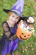 Young girl outdoors in witch costume on Halloween holding candy
