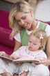 Photo: Mother in living room reading book with baby smiling Mother in living room reading book with baby smiling