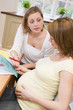 Photo: Pregnant woman in kitchen with friend reading pamphlet Pregnant woman in kitchen with friend reading pamphlet