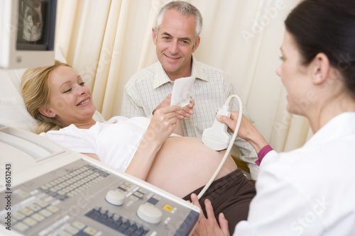 Photo: Pregnant woman getting ultrasound from doctor with husband looki Pregnant woman getting ultrasound from doctor with husband looki